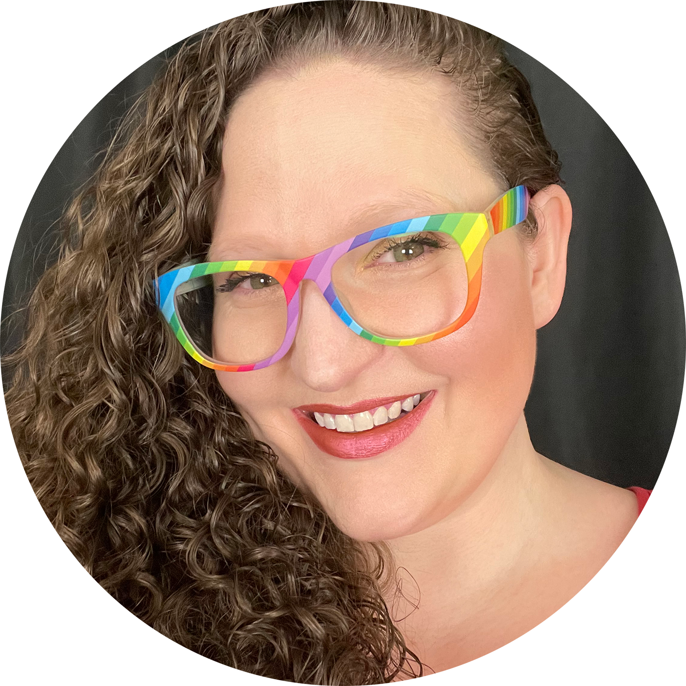 Ceemo Founder & CEO Heather Lawver, a white woman, smiles broadly at the viewer. She has excessively curly reddish brownish hair and is wearing rainbow glasses.