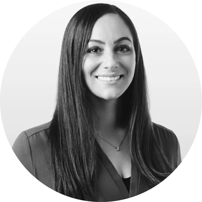 A black & white portrait of Krystin DeVita, a white woman smiling at the viewer wearing a black blouse, with long brown hair.