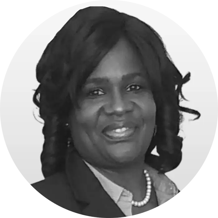 A black & white portrait of Sonja Felton, an African American woman smiling at the viewer, wearing a black blazer white button-down shirt, and a lovely string of pearls. She has shoulder-length wavy black hair.